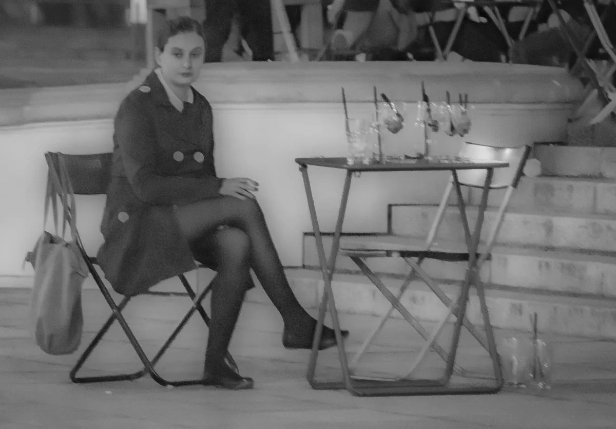 Woman sitting alone beside an empty cafe table at night